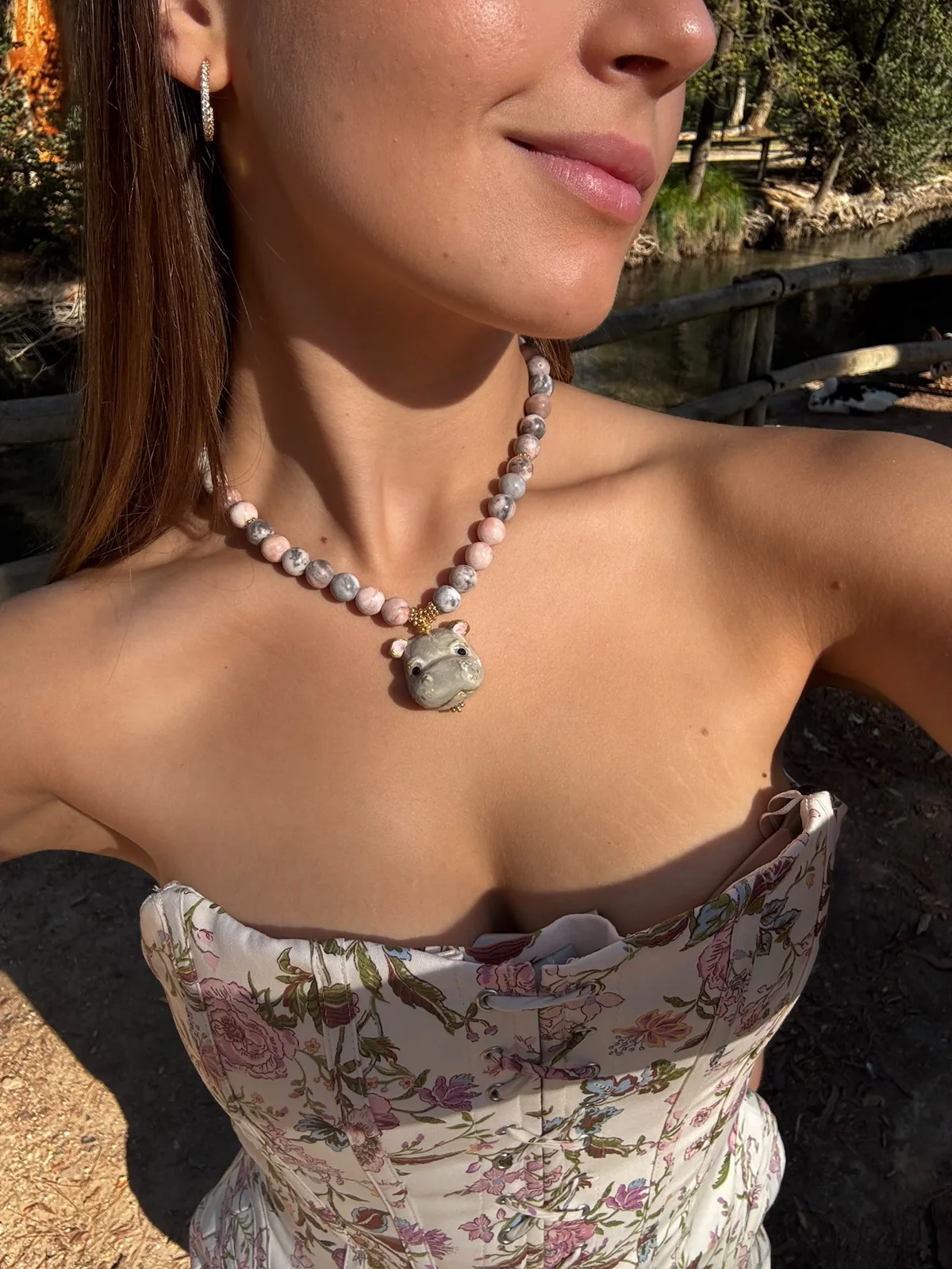 Mujer con collar de hipopótamo de cerámica pintado a mano y cuentas rosas y grises, con corsé de flores