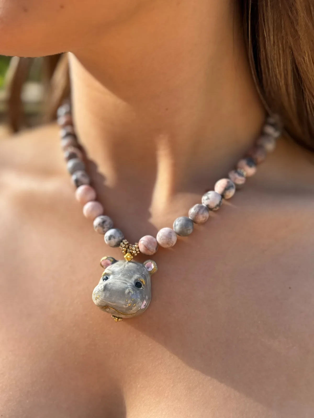 Detalle del collar hipopótamo de cerámica pintado a mano con cuentas rosas y grises, puesto